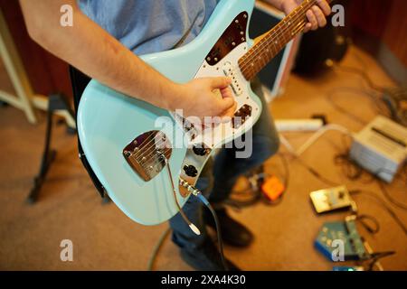 A close-up of a person playing an electric guitar, focusing on the hands strumming the strings and the guitar's body. Stock Photo