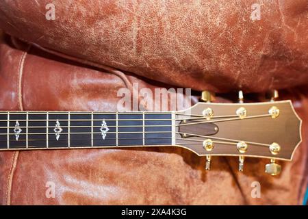 A close-up of a guitar's headstock and fretboard resting against a textured brown leather couch. Stock Photo