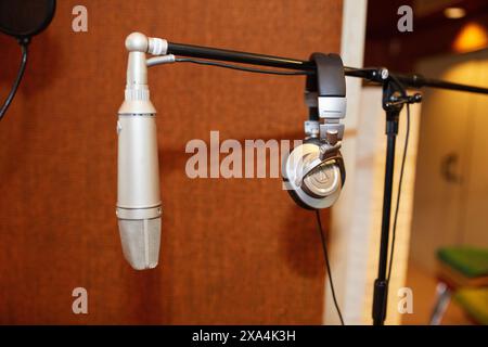 A studio microphone and headphones are mounted on stands against a blurred background with warm tones. Stock Photo