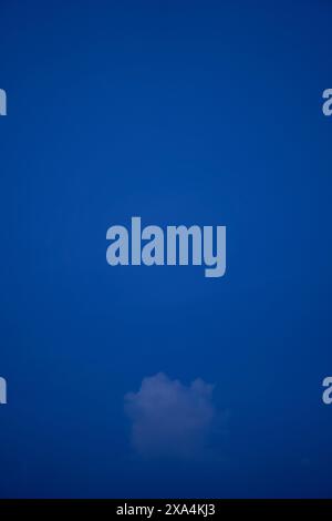 A single, small white cloud floats in a vast, deep blue sky. Stock Photo