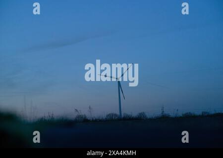 A single wind turbine stands against a twilight sky with a gradient from orange to deep blue, power lines faintly visible in the background. Stock Photo