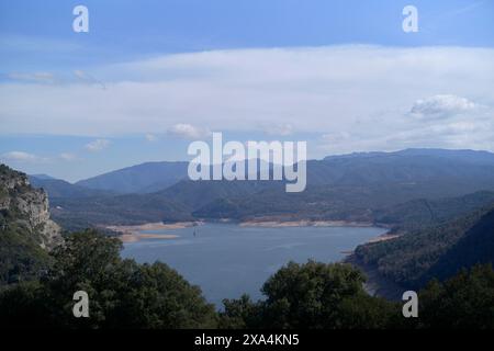 A scenic view overlooking a reservoir surrounded by mountains under a cloudy sky. Stock Photo