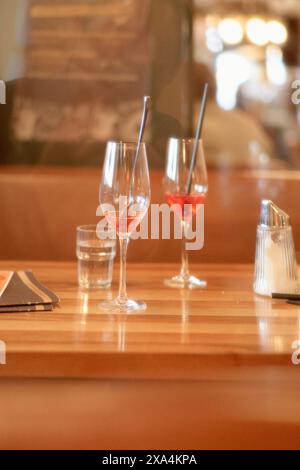 Two wine glasses, one partially filled with rose wine, sit on a wooden bar counter accompanied by a glass of water and a salt shaker, with a blurred background suggesting a cozy restaurant setting. Stock Photo