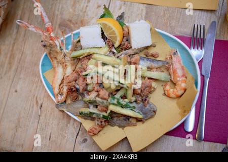 A plate of assorted seafood and vegetables, including shrimp, squid, and zucchini, displayed on a wooden table. Stock Photo