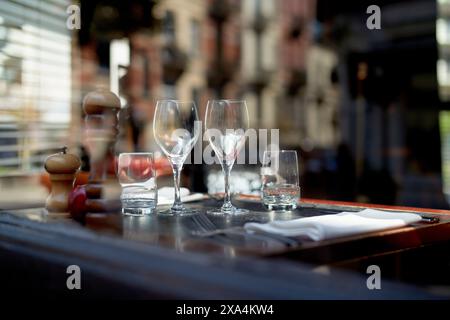 A well-set dining table on an outdoor patio with two empty wine glasses, a water glass, cutlery, and condiments, ready for guests. Stock Photo