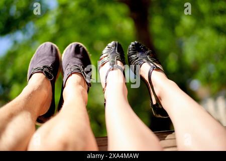 Four legs wearing shoes are extended against a blurred background of lush green foliage. Stock Photo