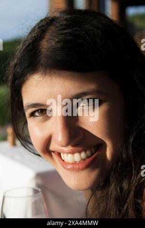 Smiling woman with dark hair enjoying a sunny day outdoors with a drink Stock Photo