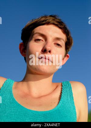 Close-up portrait of a short-haired young woman looking at the camera with a clear blue sky in the background. Stock Photo