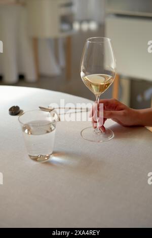 Hand holding a glass of white wine at an elegant table setting Stock Photo