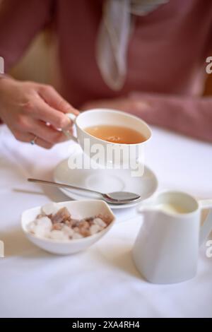 Elegant tea time with a person enjoying a cup of tea, complete with milk and sugar on the side. Stock Photo