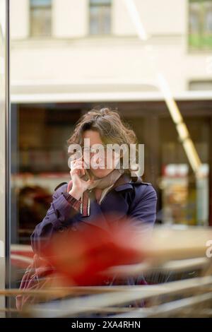 Woman talking on the phone through a cafe window, deep in thought. Stock Photo