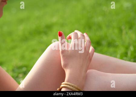 Close-up view of a person's hands resting on their knees, with one hand adorned with red nail polish. Stock Photo