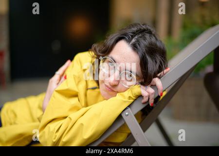 Smiling woman in yellow jacket resting on a chair Stock Photo