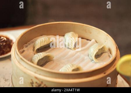 Steamed dumplings in a bamboo basket with dipping sauce on the side. Stock Photo