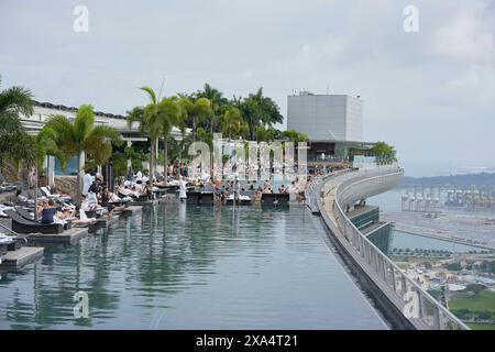 Infinity pool at a luxury resort with a scenic city and ocean backdrop, featuring guests lounging and swimming. Stock Photo