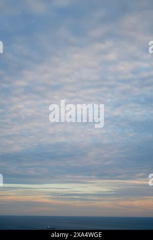 Sunset sky with altocumulus clouds over a calm ocean with a visible ship on the horizon. Stock Photo