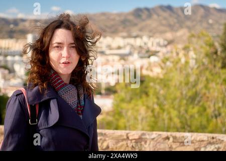 Woman with windblown hair stands in front of a scenic cityscape on a sunny day. Stock Photo