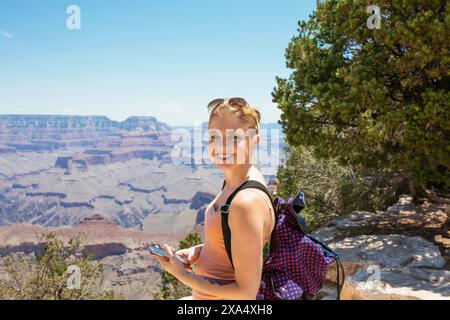 Smiling woman with a backpack standing at the Grand Canyon on a sunny day. Stock Photo