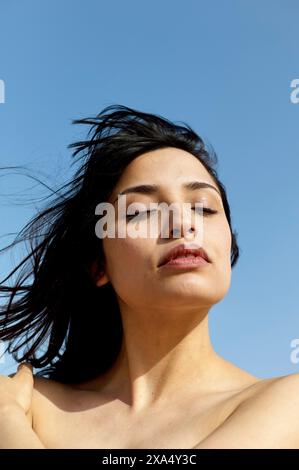 A serene woman with dark hair enjoys a calm moment under a clear blue sky. Stock Photo