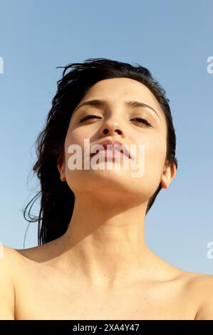 Close-up portrait of a serene woman with her hair blowing gently in the breeze and a clear blue sky in the background. Stock Photo