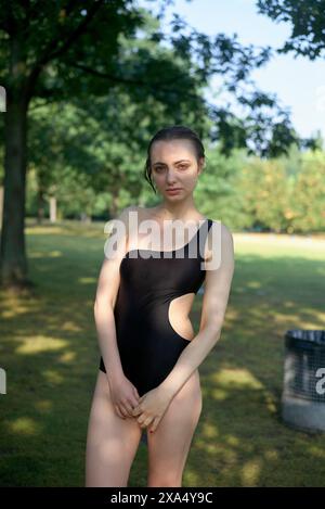 Confident young woman standing in a park wearing a black one-piece swimsuit. Stock Photo