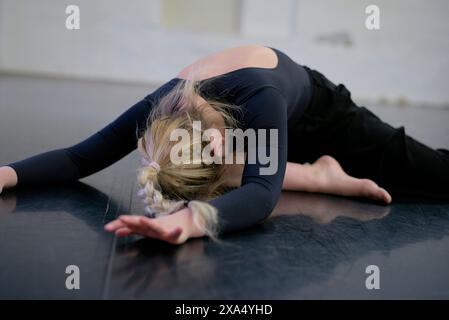 Young female dancer resting with her head down on a mat in a dance studio. Stock Photo