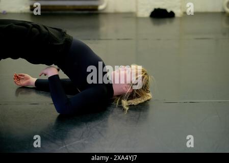 Woman practicing a bridge pose on a black mat in a dance studio. Stock Photo