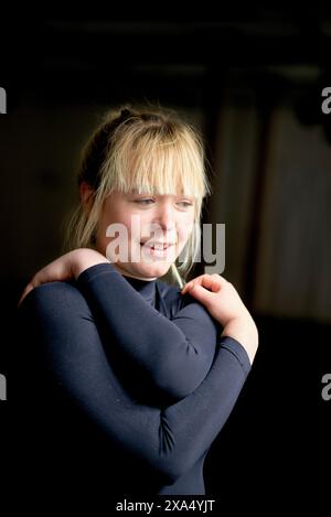 Smiling young woman with blonde hair wearing a dark top looking to the side. Stock Photo