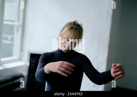 Woman in a black top stretching her arms in a brightly lit room. Stock Photo