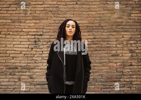 Portrait of a young beautiful woman with dreadlocks standing against a brick wall on the street. Stock Photo