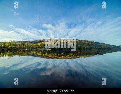 A serene lake reflecting the clear blue sky and autumn-colored trees on a tranquil day. Loch Lochy Stock Photo