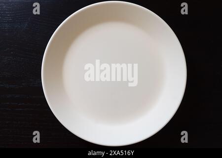 Empty white plate on black wooden table. Kitchen tools close up Stock Photo
