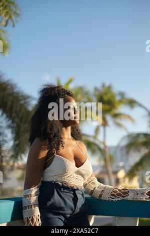 Woman relaxing on a bench with palm trees in the background during a sunny day. Stock Photo