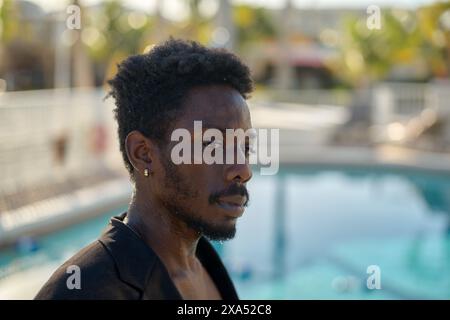 Close-up of a pensive man with a beard standing by a poolside, with his gaze focused off-camera. Stock Photo