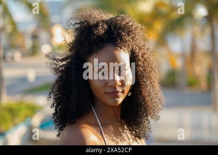 Portrait of a young woman with curly hair enjoying the golden hour sunlight outdoors. Stock Photo