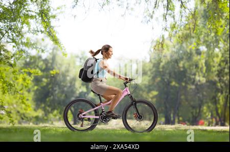 Full length profile shot of a woman with a backpack riding a bicycle in a park Stock Photo