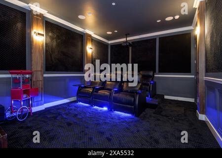 Blue lit home theater with black leather sofa and red cart Stock Photo