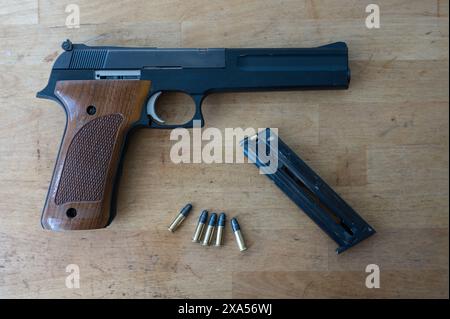 A nice classic .22 caliber pistol, a loaded magazine and a few standard bullets on the wooden table Stock Photo