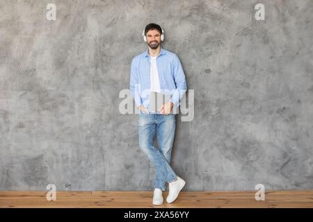 Smiling Man Leaning Against Concrete Wall With Laptop and Headphones Stock Photo