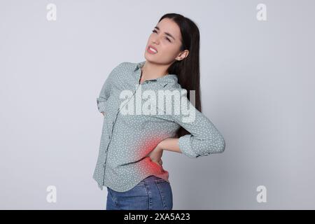 Woman suffering from back pain on light background Stock Photo