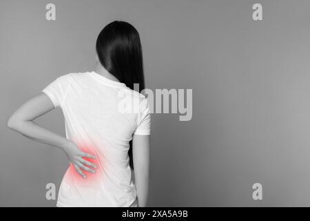 Woman suffering from back pain on grey background. Black and white effect with red accent Stock Photo