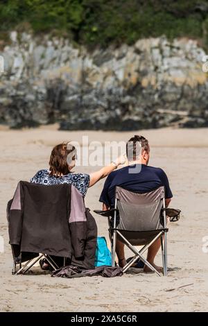 A couple sitting on camping chairs and enjoying the sunshine on Crantock Beach in Newquay in Cornwall in the UK. Stock Photo