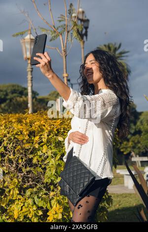 A Woman is taking a selfie with her cell phone wearing a black and clothes. She is smiling and she is enjoying herself, vertical image. Stock Photo
