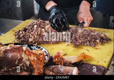 male chef cut boiled lamb meat with knife to cook Uzbek pilaf in a restaurant in Central Asian Pilaf Center in Tashkent in Uzbekistan Stock Photo