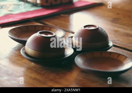 Close up view of a set of handmade brown earthen cups with simple ethnic design for tea or coffee resting on a wooden table, exuding cozy rustic charm Stock Photo
