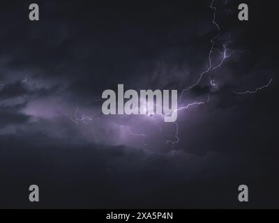Lightning bolts illuminate the stormy night sky, approaching the viewer Stock Photo