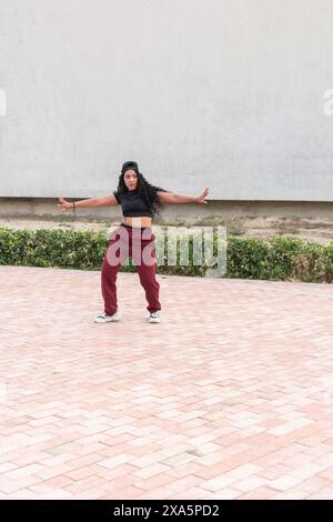 Young woman in casual athletic wear striking a hip-hop dance pose outdoors. Stock Photo