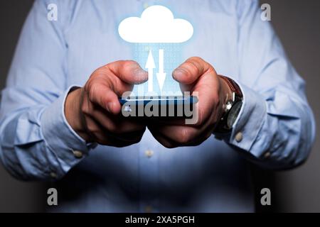 Close-up of a unrecognizable man's hands holding a mobile phone with a icon of a cloud over it and two arrows symbolizing data transfer. Stock Photo