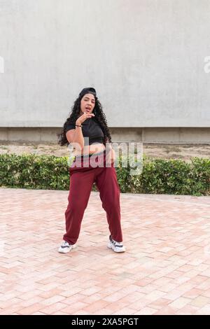 Young woman in casual athletic wear posing confidently in hip-hop dance style outdoors. Stock Photo