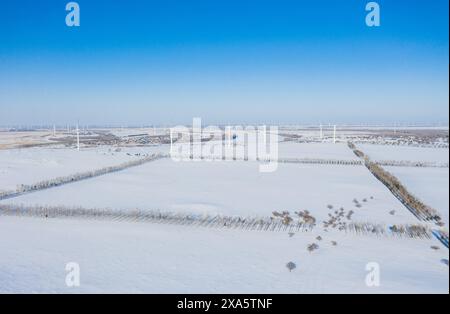 A snowy field with a windmill and barbed wire fence Stock Photo